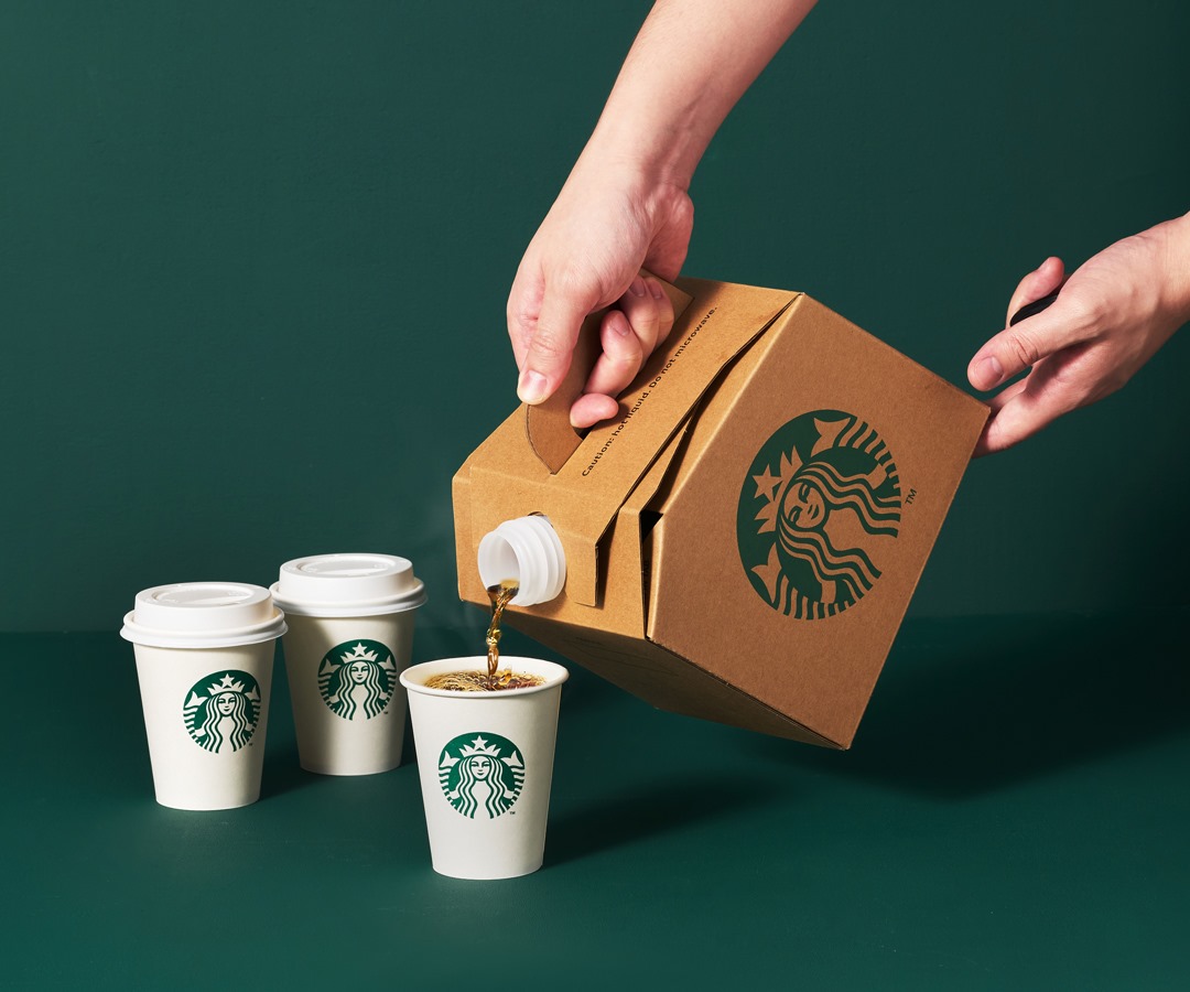 A man's hands are seen as he accidentally spills coffee from a Starbucks coffee traveler, which contains three on-the-go cups.